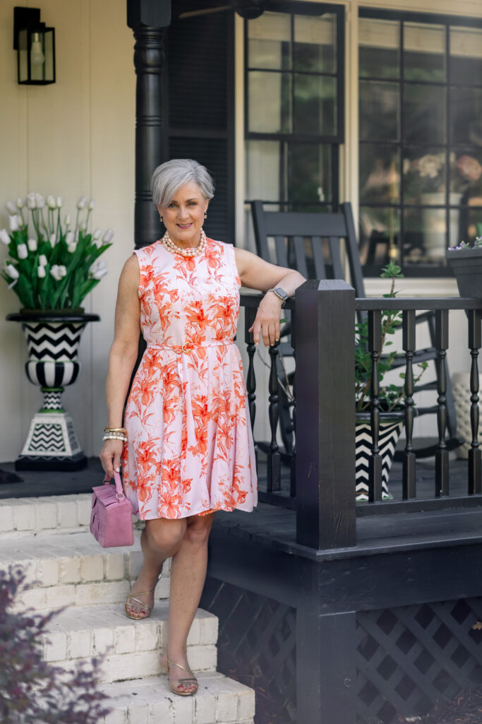 Pink sleeveless dress with orange floral print, pearl necklace, and pink suede bag