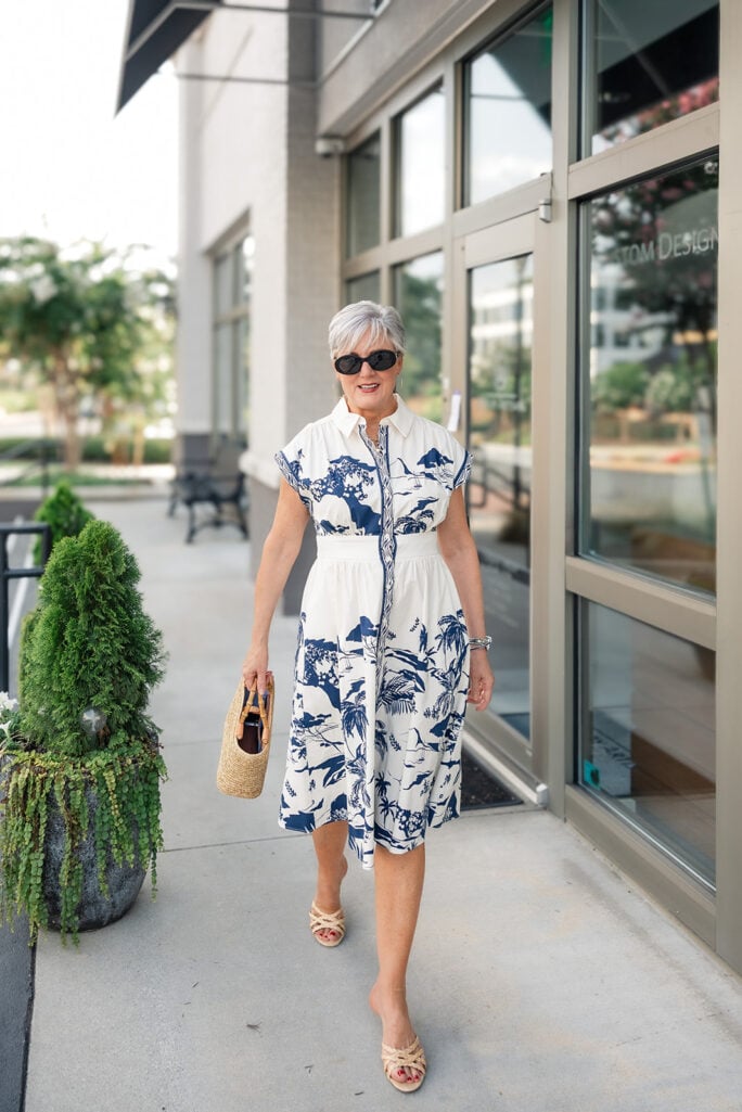 Woman wearing a navy and white toile print shirtdress with a straw bamboo-handle bag, fall transition style