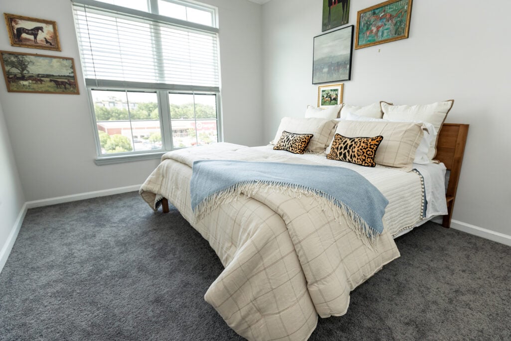Guest bedroom with layered neutral bedding, a blue throw, leopard-print pillows and a framed gallery wall