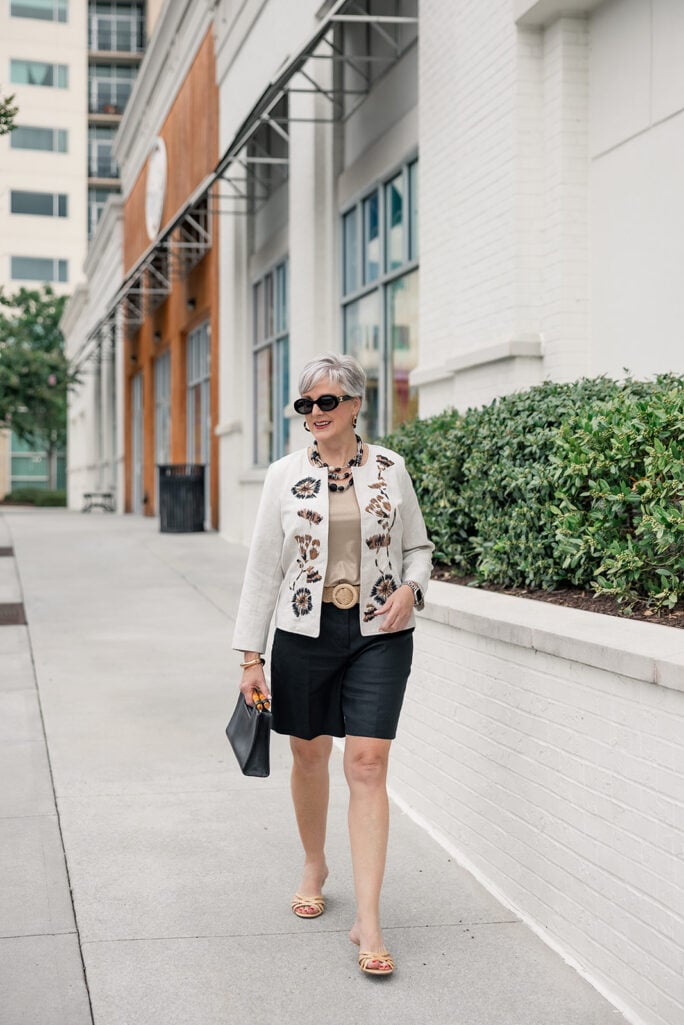 Beth Djalali in an embroidered linen jacket and black linen shorts with raffia kitten heels — a low comfortable heel lengthening the leg line