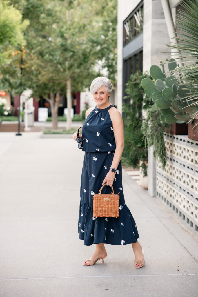 Over 50 fashion blogger styling a navy floral embroidered two-piece set with a woven wicker handbag and kitten heel sandals for summer.