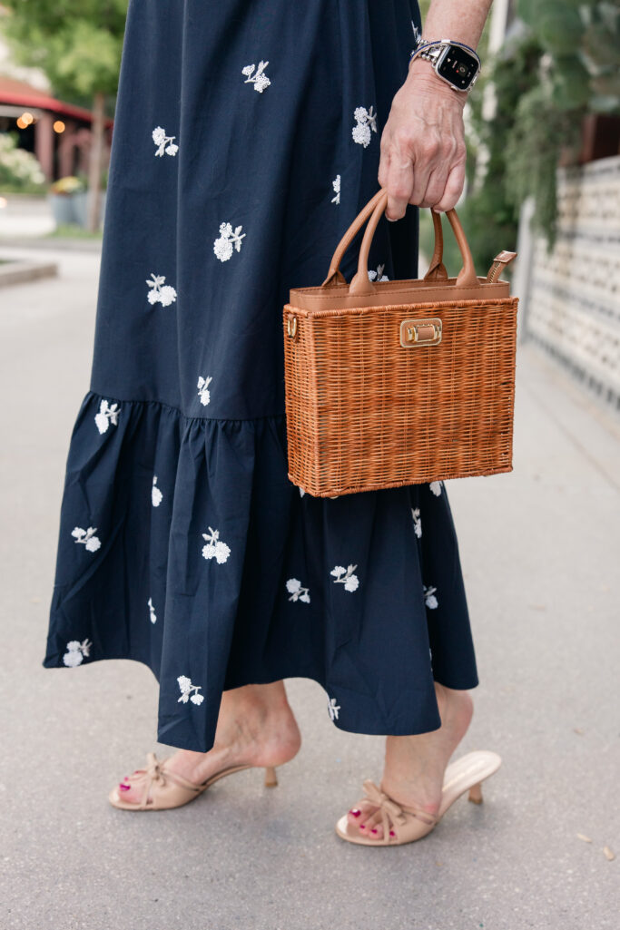 Close-up detail of white floral embroidery on a navy Ann Taylor bubble hem halter top with a wicker top-handle handbag.