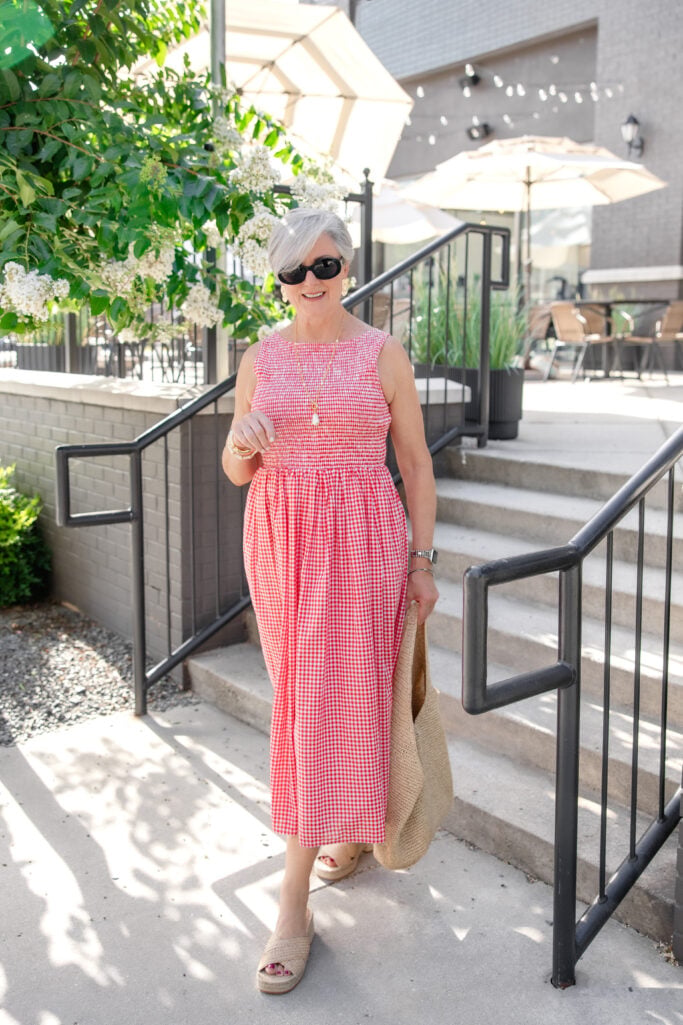 Beth wearing a red gingham midi sundress with a smocked bodice, platform espadrilles, and a straw tote