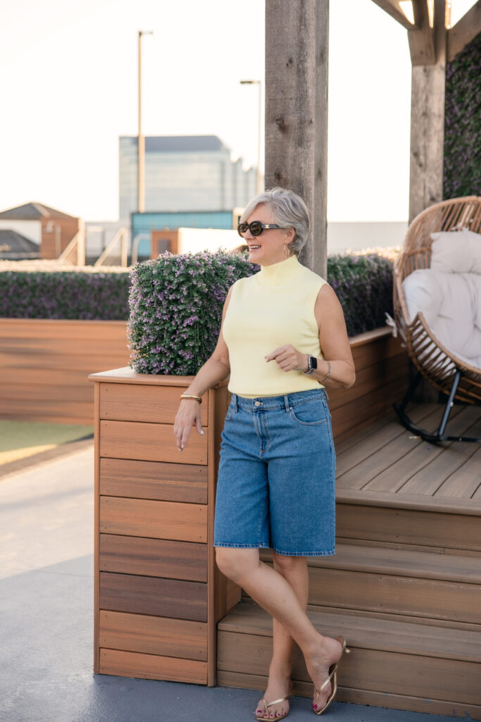 Butter yellow sleeveless mock-neck top styled with light rinse denim Bermuda shorts and gold sandals