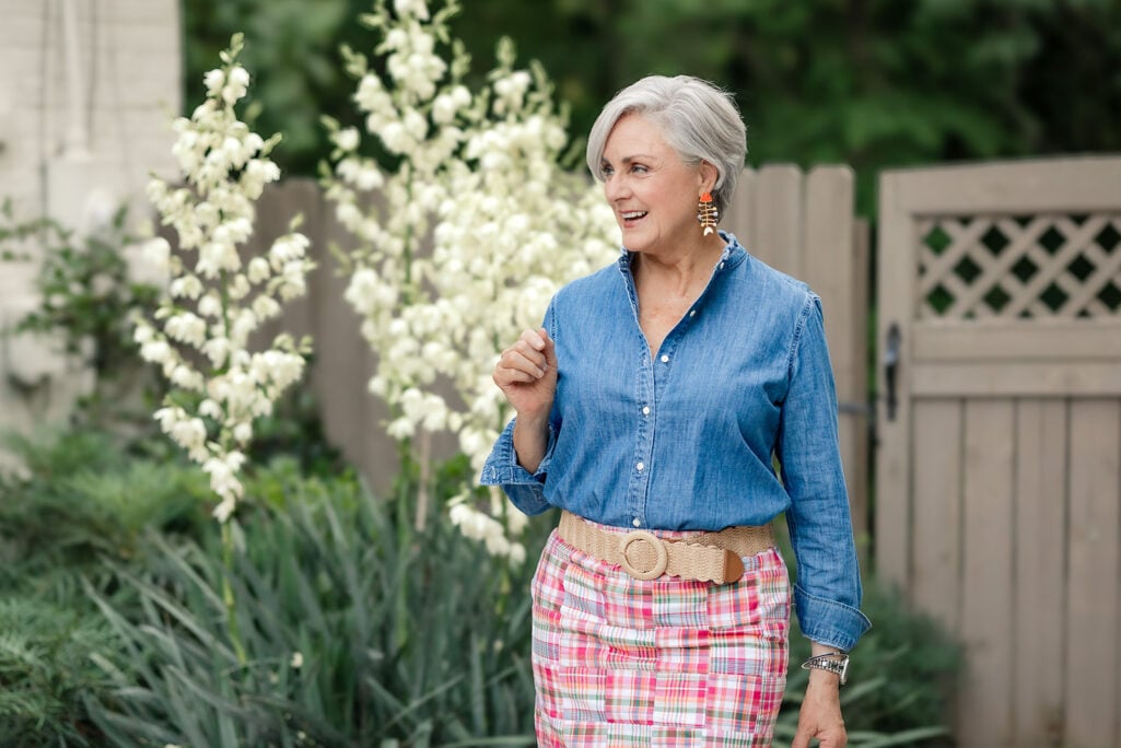 Beth wearing whimsical orange and white beaded fish-shaped statement earrings, styled with a chambray button-down shirt, pink and green patchwork madras skirt, and a woven raffia belt.