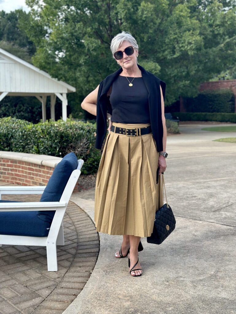 Black top with khaki pleated midi skirt and black belt, a summer color combination for women over 50