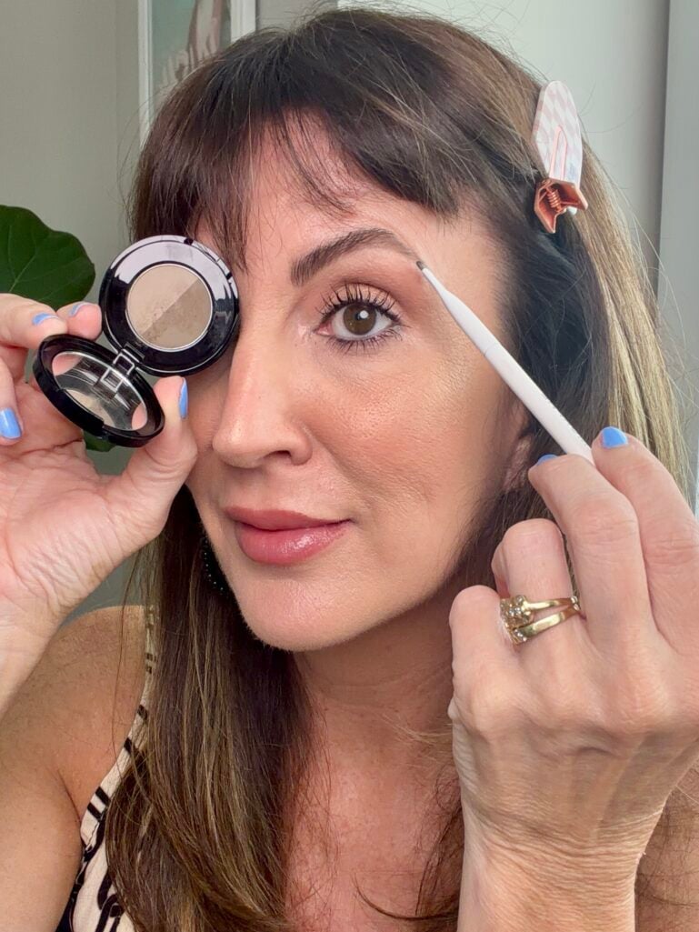 Filling in brows with powder for a fuller, youthful shape.