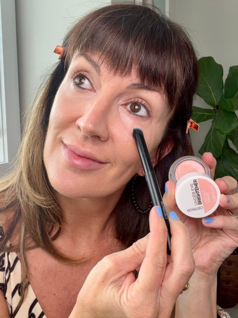 : Applying pink-toned concealer to brighten under-eyes over 50.